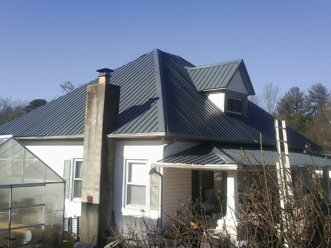 Dark blue standing seam metal roof on a white farmhouse with dormer — Slate & Tile Roof Repair by Roofing Brothers in Tatum