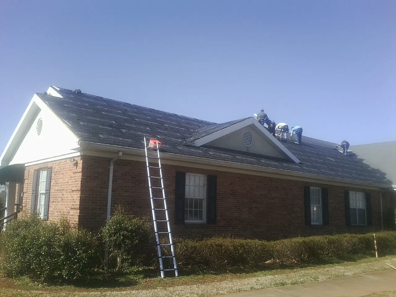 Crew tearing shingles off a brick ranch roof with a ladder set — Emergency Roof Repair work by our crew in Tatum