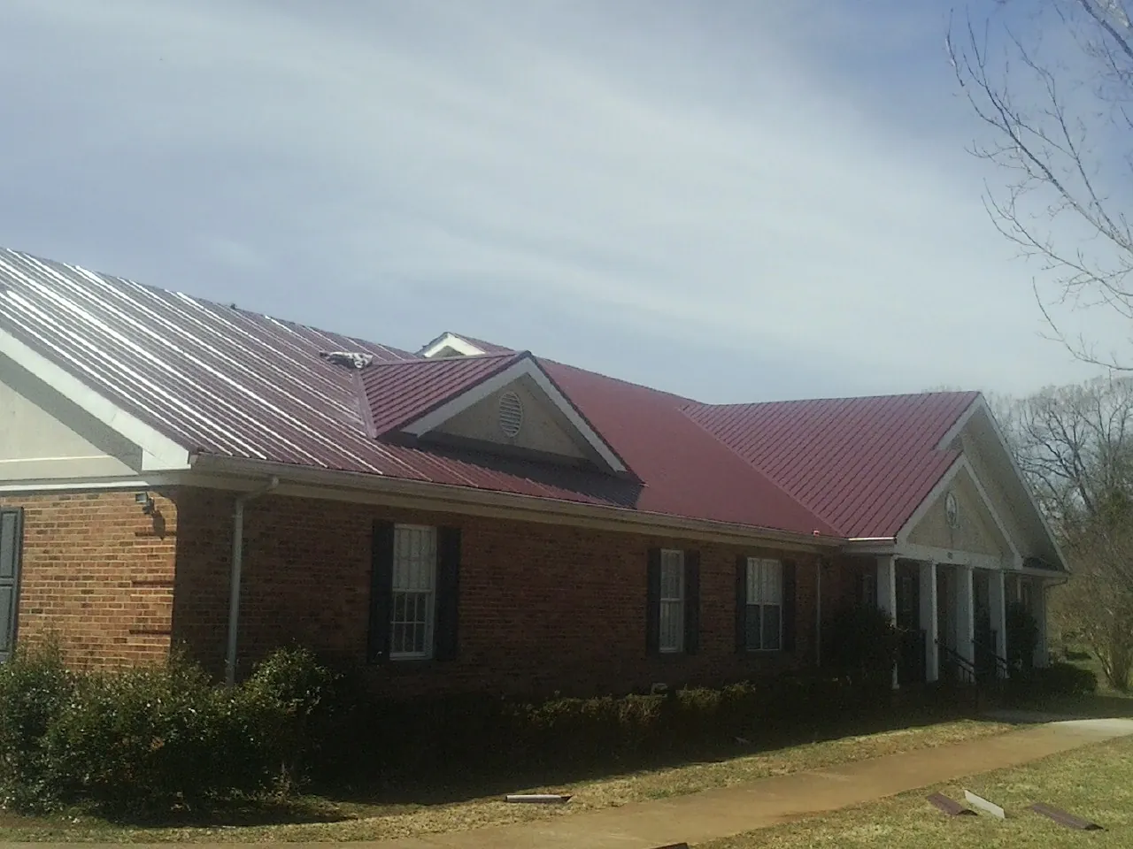 Red metal roof with gabled entries on a long brick building, from a Hail Damage Roof Repair job in Tatum