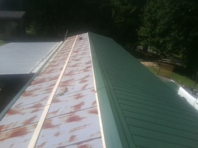 Old rusted panels beside newly installed green metal roofing — Wind Damage Roof Repair by Roofing Brothers in Tatum
