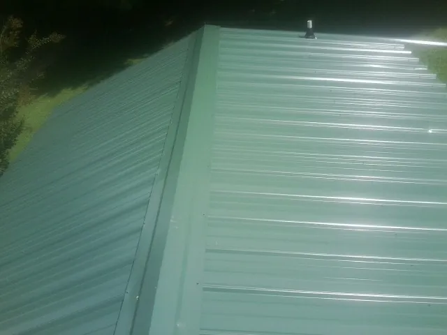 New green metal panels meeting at the ridge of a roof — Flat Roof Repair work by our crew in Tatum