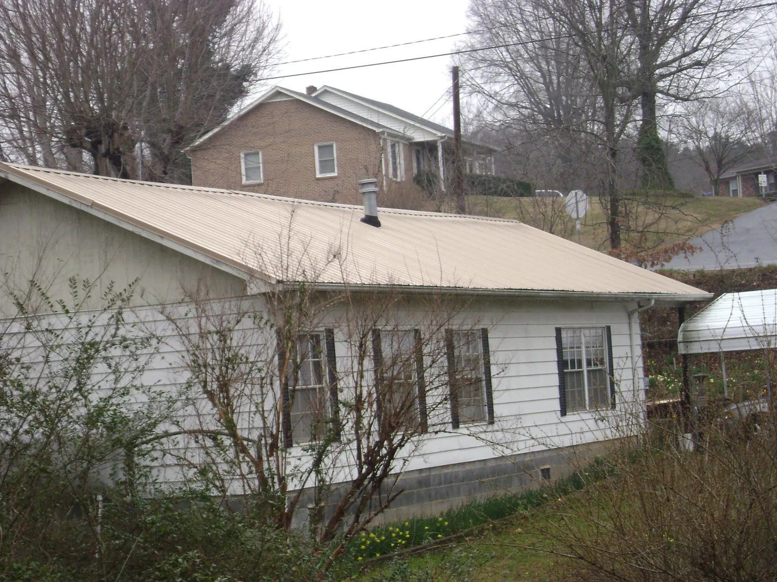 Tan metal roof on a white sided house set into a hillside — Commercial Roofing by Roofing Brothers in Tatum